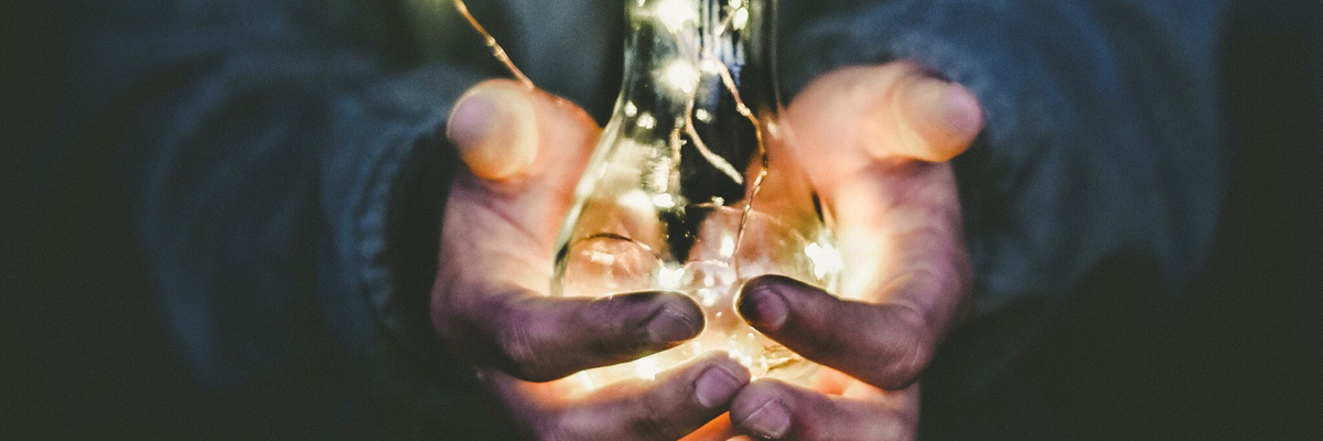 Två händer som håller i en glödlampa med små ljus symboliserande kreativitet och innovation